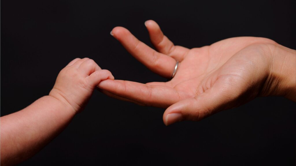 A newborn baby reaching out to touch a parent's hand